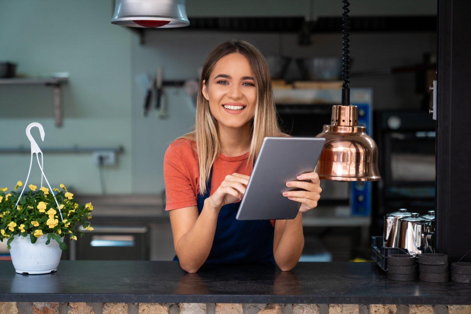 Smiling confident young woman wearing apron looking at camera holding digital tablet